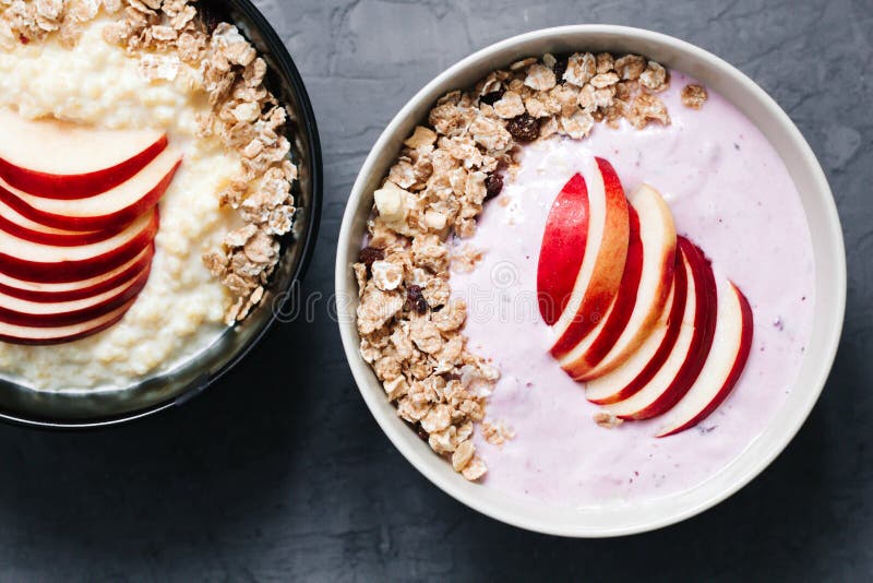 Cuenco de gachas de avena de la harina de avena con el yogur de arándano, la leche y el muesli con una manzana en fondo concreto imagen de archivo Cuenco de gachas de avena de la harina de avena con el yogur de arándano, la leche y el muesli con una manzana en fondo concreto imagen de archivo
