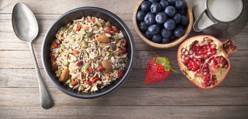 A bowl of healthy granola or muesli cereal with blueberries, strawberries and pomegranate on a rustic wood background from above. A bowl of healthy granola or muesli cereal with blueberries, strawberries and pomegranate on a rustic wood background from above