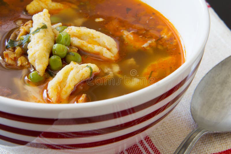 Cuenco de sopa rumana del pollo y de la bola de masa hervida con los guisantes en mantel rayado rojo hecho a mano de lino antiguo foto de archivo Cuenco de sopa rumana del pollo y de la bola de masa hervida con los guisantes en mantel rayado rojo hecho a mano de lino antiguo foto de archivo