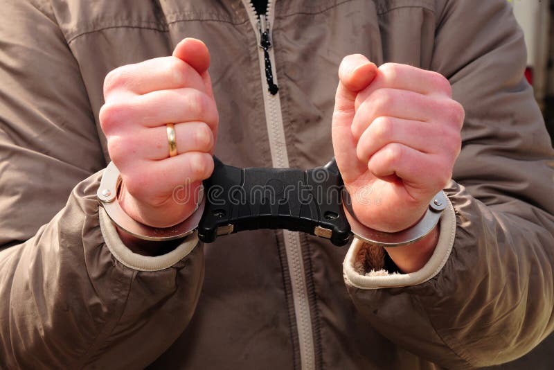 A suspect is detaind by police, his wrists secured by handcuffs. A suspect is detaind by police, his wrists secured by handcuffs.