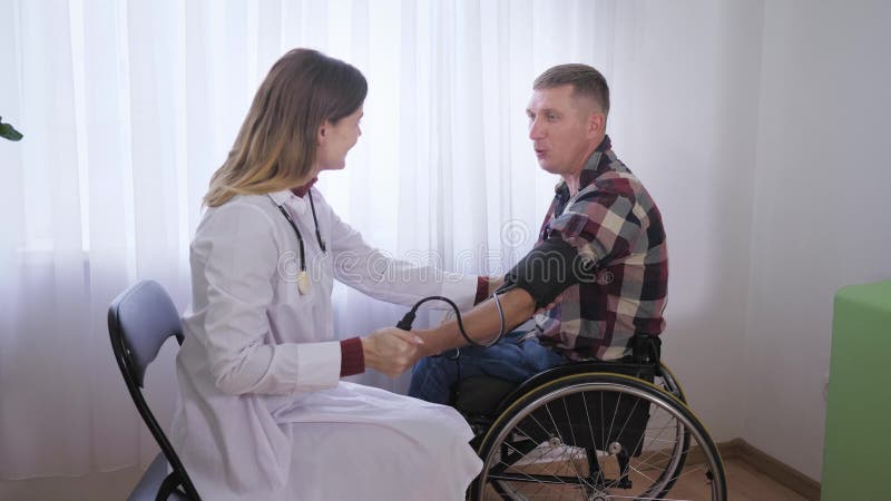 Cuidados de saúde, um paciente em cadeira de rodas examina médico mede a pressão para ele com um dispositivo médico