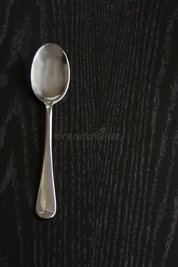 A simple rat-tail design silver spoon on a black wooden background. A simple rat-tail design silver spoon on a black wooden background