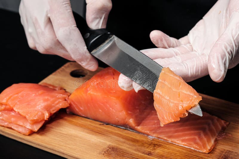 cuisiniers de mains en gros plan Le chef coupe avec un couteau un poisson rouge, saumons fumés sur une planche à découper en bois photographie stock libre de droits cuisiniers de mains en gros plan Le chef coupe avec un couteau un poisson rouge, saumons fumés sur une planche à découper en bois photographie stock libre de droits