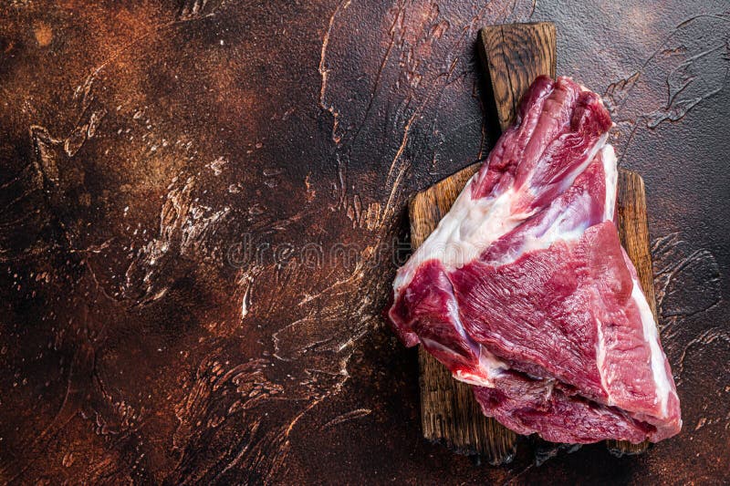 Raw lamb mutton thigh on butcher table. Dark background. Top view. Copy space. Raw lamb mutton thigh on butcher table. Dark background. Top view. Copy space.