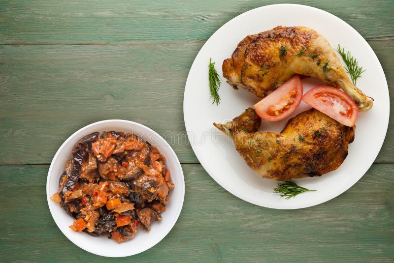 Chicken thigh with vegetables salad on a green wooden background. chicken leg on a plate. Chicken thigh with vegetables salad on a green wooden background. chicken leg on a plate