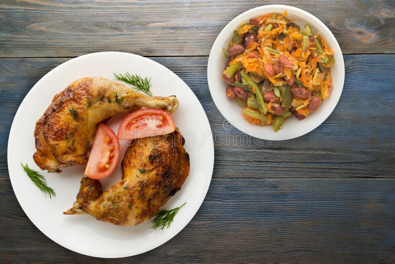 Chicken thigh with vegetables salad on a blue wooden background. chicken leg on a plate. Chicken thigh with vegetables salad on a blue wooden background. chicken leg on a plate