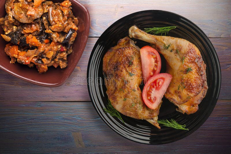 Chicken thigh with vegetables on purple wooden background. chicken leg on blac plate with vegetable salad top view. Chicken thigh with vegetables on purple wooden background. chicken leg on blac plate with vegetable salad top view