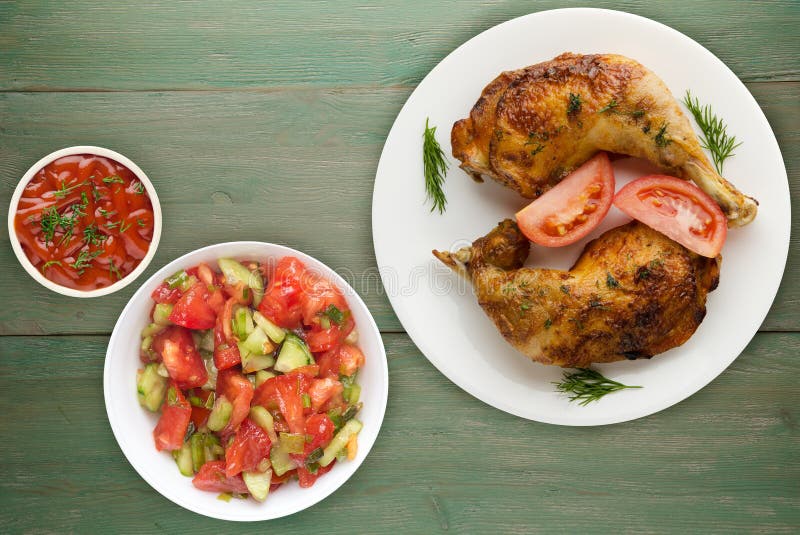 Chicken thigh with vegetables salad on a green wooden background. chicken leg on a plate. Chicken thigh with vegetables salad on a green wooden background. chicken leg on a plate