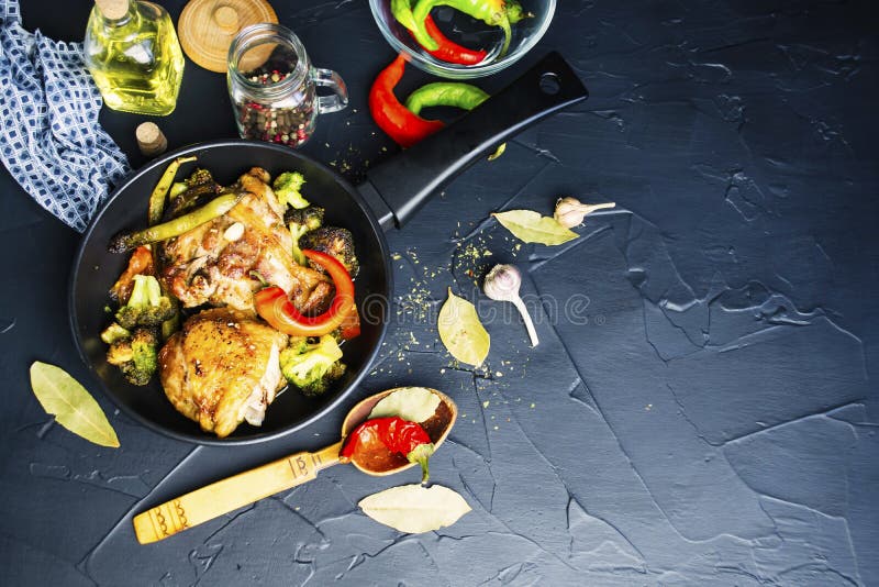 Fried chicken thigh with broccoli in a spicy sauce in a pan on a black background. Fried chicken thigh with broccoli in a spicy sauce in a pan on a black background