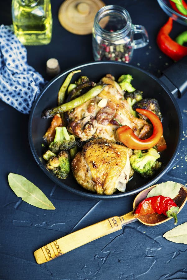 Fried chicken thigh with broccoli in a spicy sauce in a pan on a black background. Fried chicken thigh with broccoli in a spicy sauce in a pan on a black background