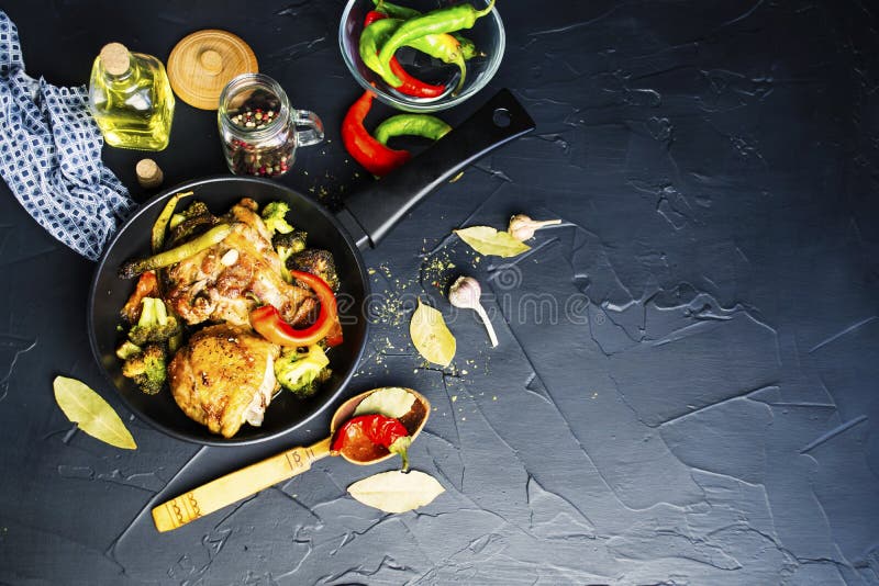 Fried chicken thigh with broccoli in a spicy sauce in a pan on a black background. Fried chicken thigh with broccoli in a spicy sauce in a pan on a black background