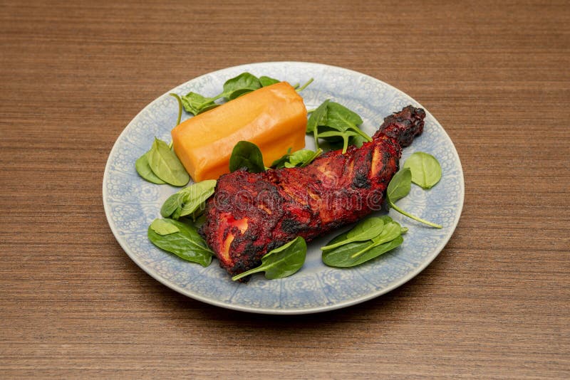 Roasted chicken thigh in Hindu tandoori style with a good piece of sweet potato garnish on a beautiful blue plate. Roasted chicken thigh in Hindu tandoori style with a good piece of sweet potato garnish on a beautiful blue plate