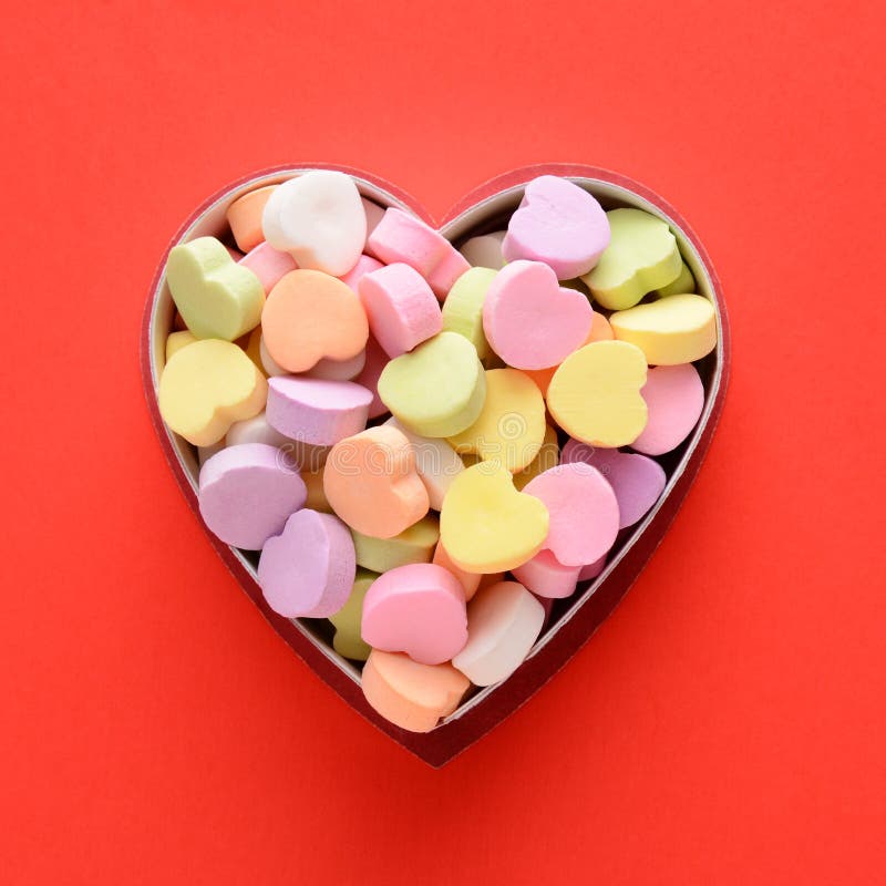 High angle view of a bunch of pastel candy hearts in a heart shaped box for Valentines Day. Square format on a red background, the candies are blank. High angle view of a bunch of pastel candy hearts in a heart shaped box for Valentines Day. Square format on a red background, the candies are blank.