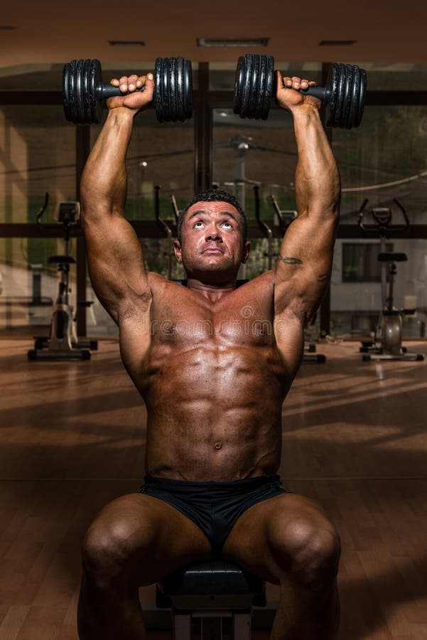 Culturista masculino que hace pesa de gimnasia de la pizca de la prensa del hombro imagen de archivo libre de regalías Culturista masculino que hace pesa de gimnasia de la pizca de la prensa del hombro imagen de archivo libre de regalías