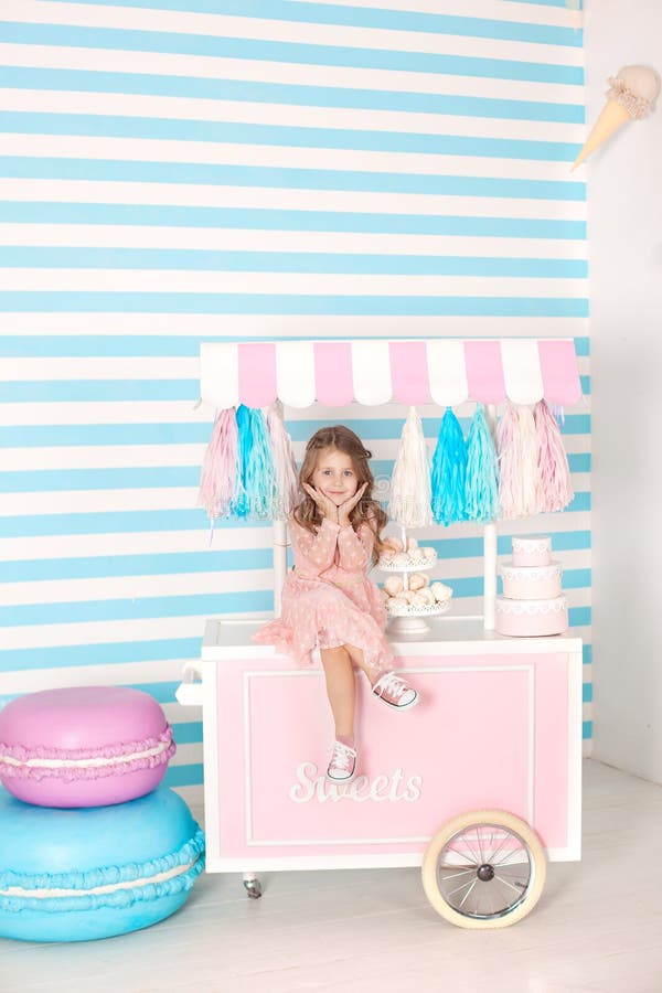 Cumpleaños y concepto de la felicidad - niña feliz que se sienta en una carretilla con helado y dulces contra la perspectiva de u fotos de archivo libres de regalías Cumpleaños y concepto de la felicidad - niña feliz que se sienta en una carretilla con helado y dulces contra la perspectiva de u fotos de archivo libres de regalías