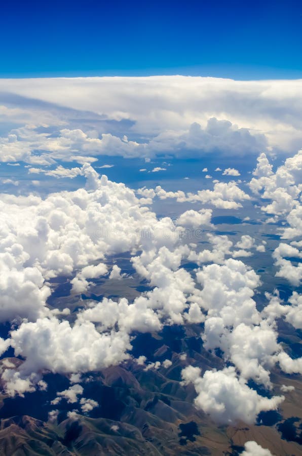 Beautiful sky background with white clouds that cast a shadow on the ground. Mountains and clouds from a height of a flying plane. Vertical frame. Airplane height stock images, royalty-free photos and pictures