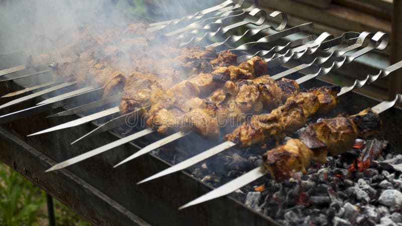 Cuochi della carne sui carboni caldi nel fumo Picnic in natura immagini stock libere da diritti Cuochi della carne sui carboni caldi nel fumo Picnic in natura immagini stock libere da diritti
