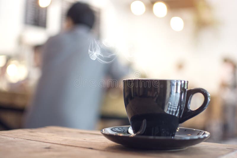 Cuocia a vapore il caffè caldo sulla tavola di legno con l'uomo vago che si siede nel caffè fotografia stock libera da diritti Cuocia a vapore il caffè caldo sulla tavola di legno con l'uomo vago che si siede nel caffè fotografia stock libera da diritti