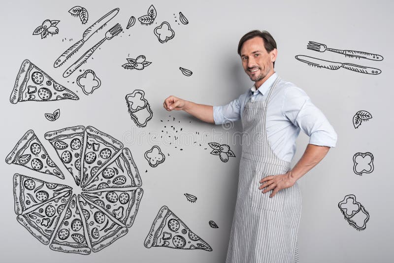 Cuoco sorridente che aggiunge le spezie mentre cucinando pizza fotografie stock Cuoco sorridente che aggiunge le spezie mentre cucinando pizza fotografie stock