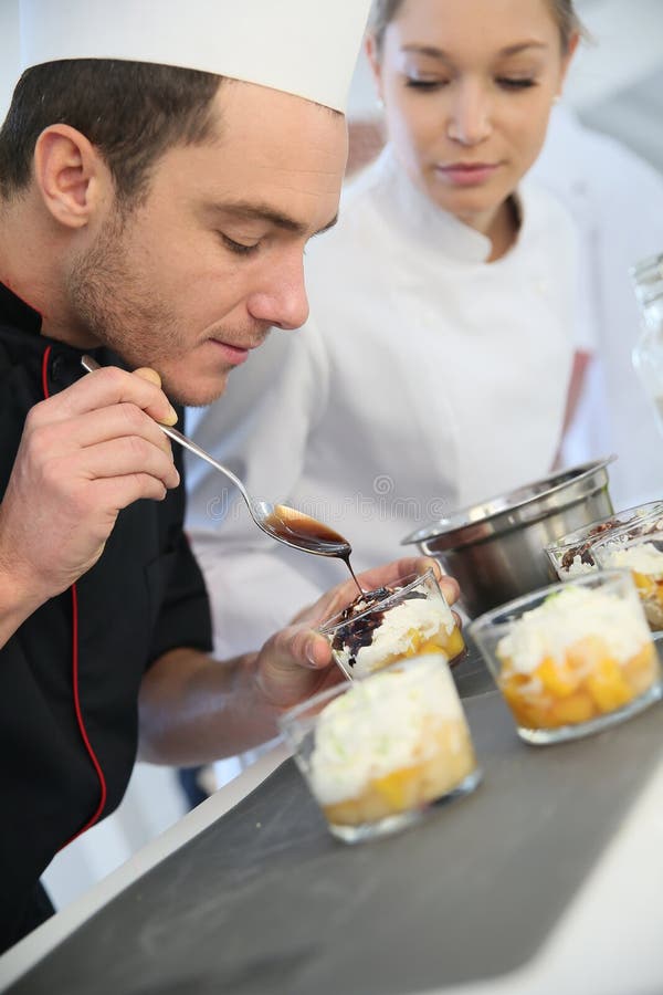 Cuoco unico con il cioccolato di versamento dello studente sul dessert fotografie stock Cuoco unico con il cioccolato di versamento dello studente sul dessert fotografie stock