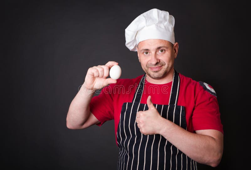 Cuoco unico con l'uovo del pollo in studio su fondo nero immagini stock libere da diritti Cuoco unico con l'uovo del pollo in studio su fondo nero immagini stock libere da diritti