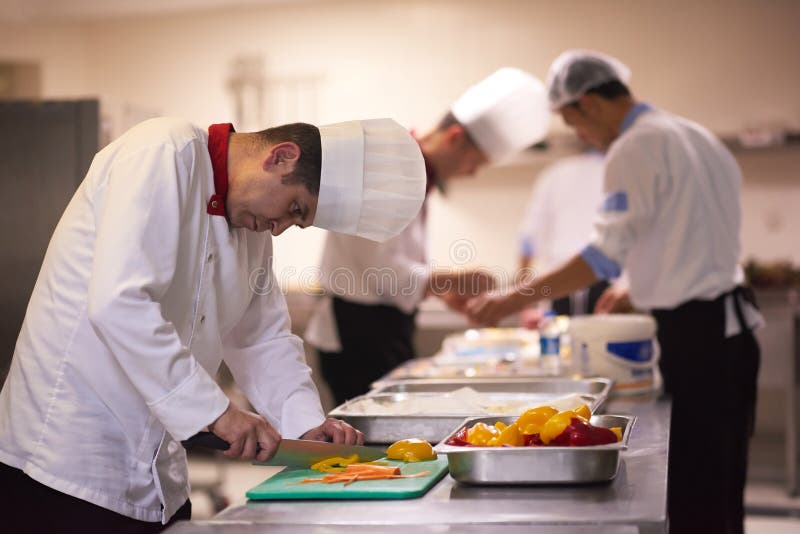 Cuoco unico nelle verdure della fetta della cucina dell'hotel con il coltello immagine stock Cuoco unico nelle verdure della fetta della cucina dell'hotel con il coltello immagine stock