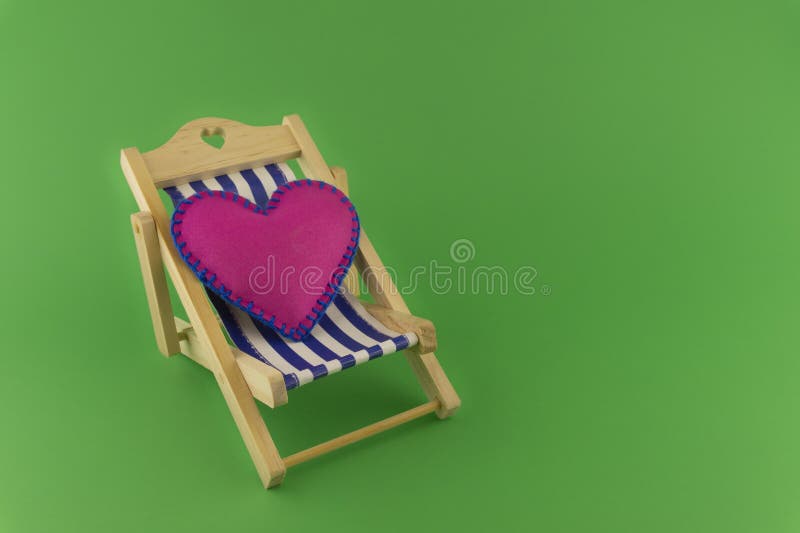 Romantic pink heart on a striped deck chair over a green background symbolic of love, an engagement, wedding or Valentines Day. Romantic pink heart on a striped deck chair over a green background symbolic of love, an engagement, wedding or Valentines Day