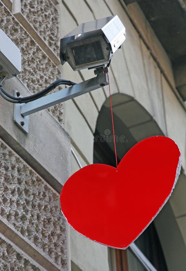 Cuore rosso che pende da una videosorveglianza di una banca immagine stock Cuore rosso che pende da una videosorveglianza di una banca immagine stock