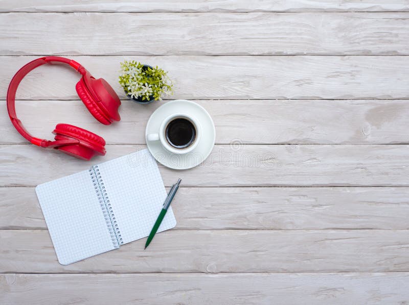 A cup of black coffee, overhead Musical headphones with a notepad with a blank page for text. Wooden desktop with a smartphone stock images