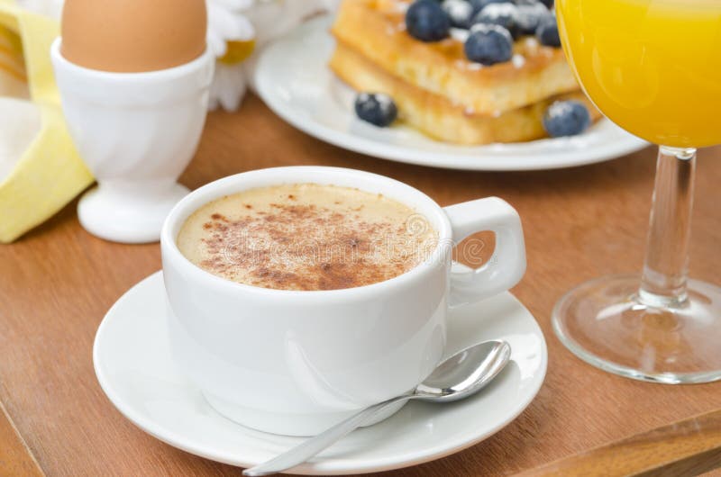 cup of cappuccino, belgian waffles with blueberries, orange juice and egg for breakfast