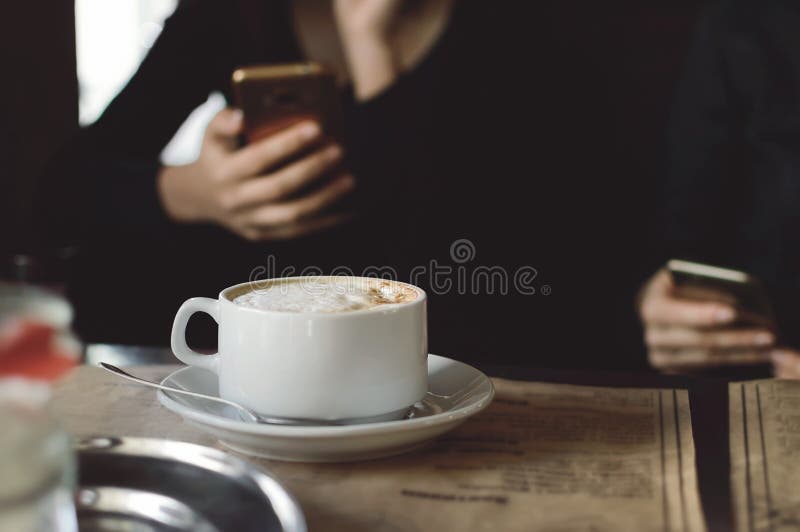 A cup of cappuccino coffee on a table in a cafe. People drink coffee in a cafe and use mobile phones. Close-up. royalty free stock photography A cup of cappuccino coffee on a table in a cafe. People drink coffee in a cafe and use mobile phones. Close-up. royalty free stock photography