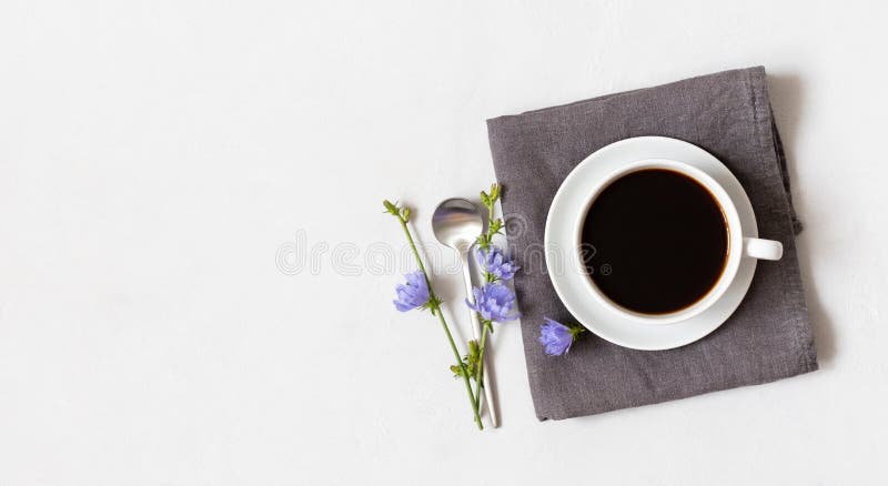Cup with chicory coffee on a gray napkin and blue flowers on a white background. Coffee substitute. Healthy drink. Copy space, top