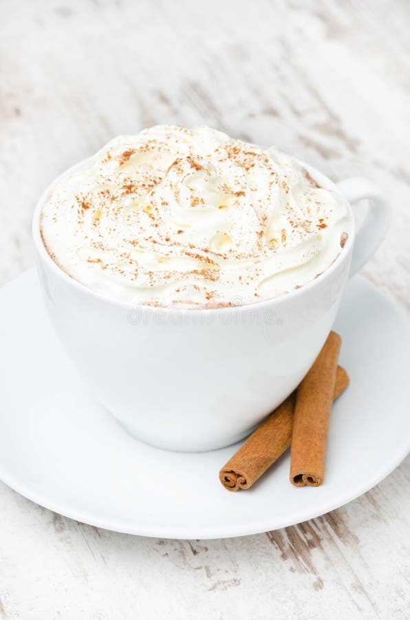 Cup of cocoa with cinnamon and whipped cream on white table