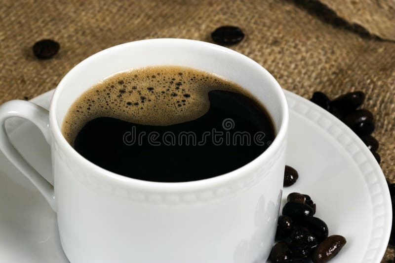Eine weiße Tasse gefüllt mit frischem französischem gedrückt Kaffee, Natürliche Jute hintergrund, ganze Kaffeebohnen verstreut auf hintergrund und auf die Untertasse.
