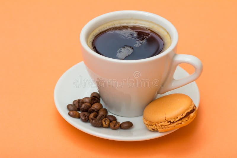 Cup of coffee with coffee beans and delicious macaron cake on peach background.