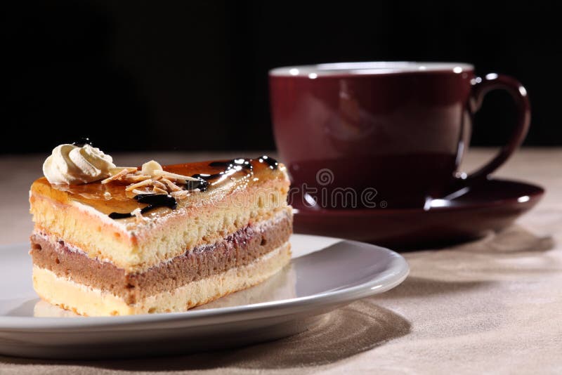 Gustosa fetta di strati di torta al caffè, su una targhetta bianca, con ciliegia nera tazza di caffè e piattino.