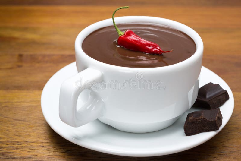 Cup of hot chocolate with chili peppers on a wooden background