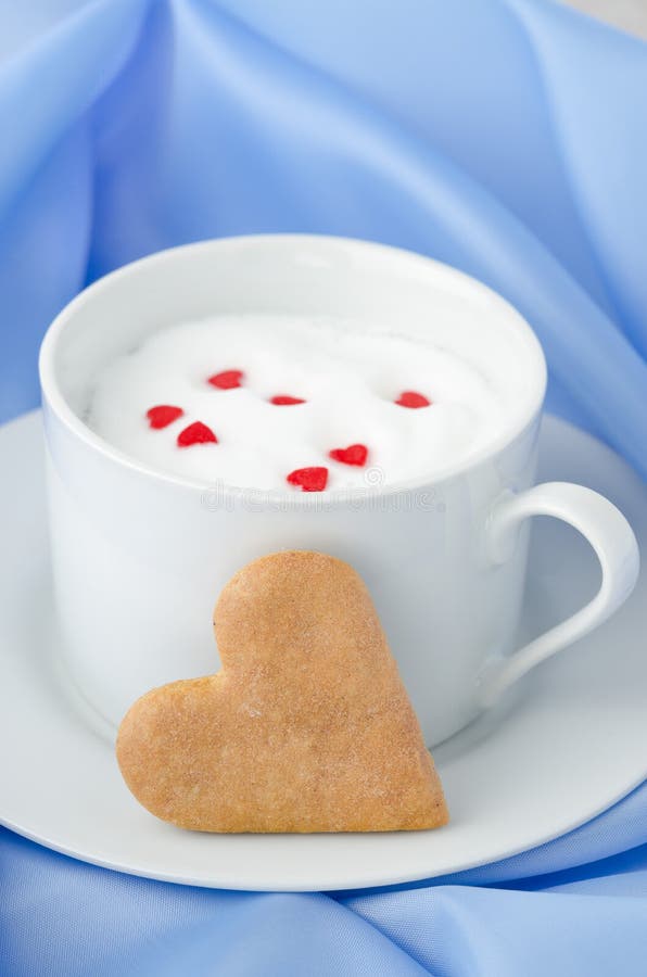 Cup of hot milk with foam, decorated with sugar hearts and heart