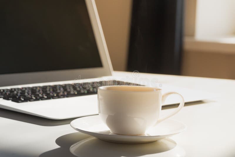 Cup of hot steaming morning coffee and laptop computer.