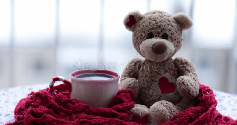 Cup of hot tea and teddy bear wrapping in red scarf on table in snow