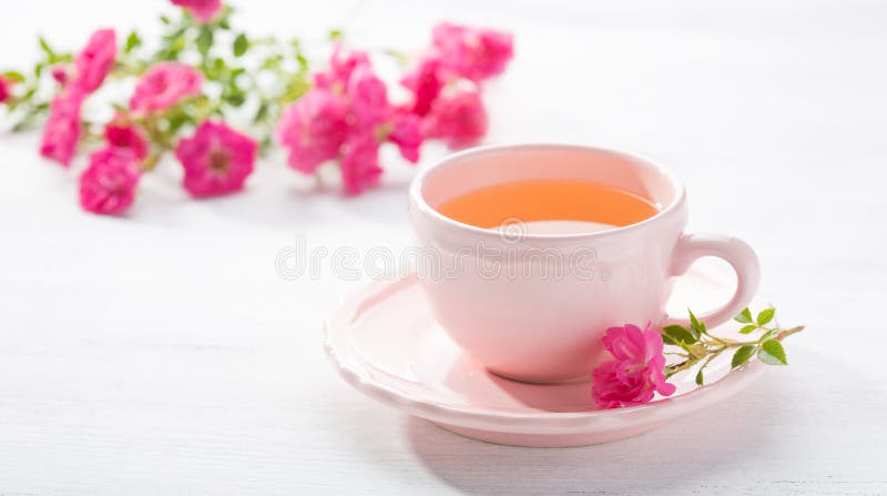 Cup of tea and branch of small pink roses on white rustic table stock photos.