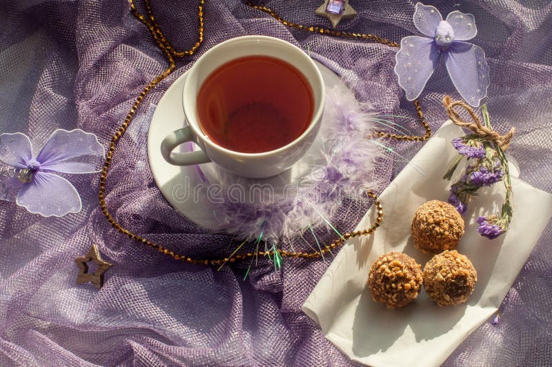 A cup of tea and chocolate sweets on a violet delicate tulle fabric