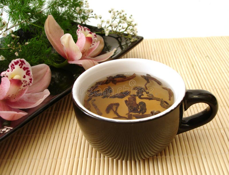 Cup of tea with pink orchids on black plate over straw matt