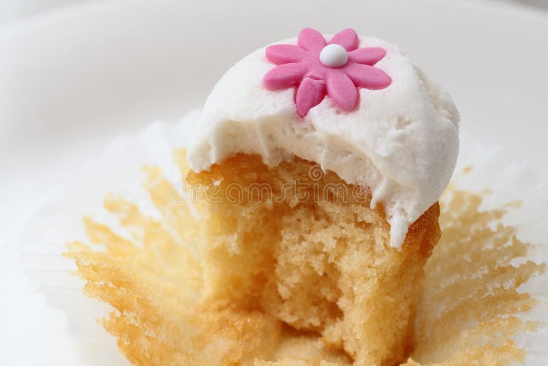 Cupcake decorated with a tiny pink flower on its creamy topping - bitten off. Cupcake decorated with a tiny pink flower on its creamy topping - bitten off