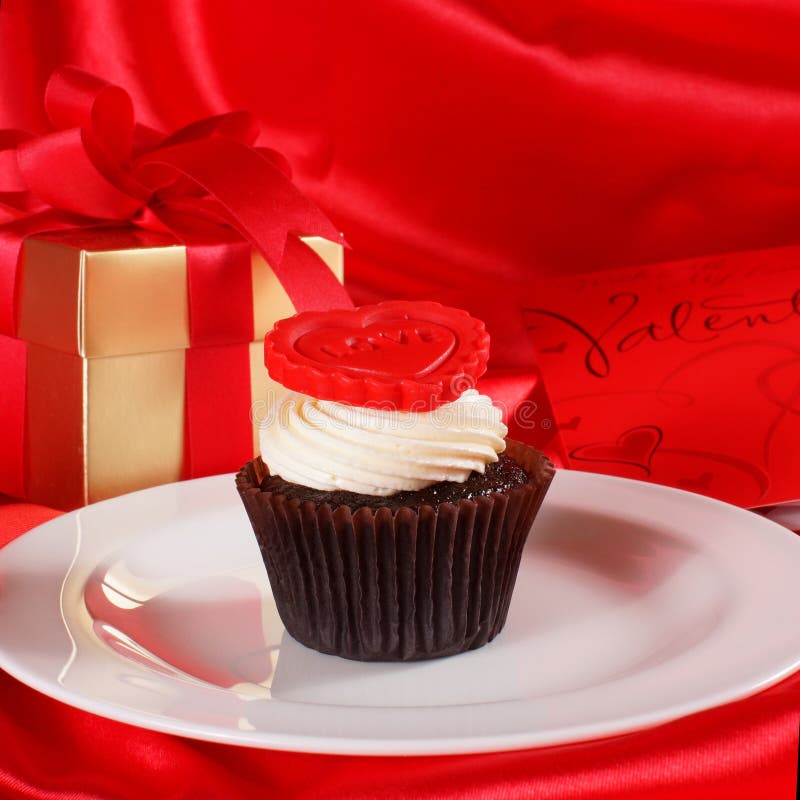 Cupcake with a red heart on top and gifts in boxes on red satin