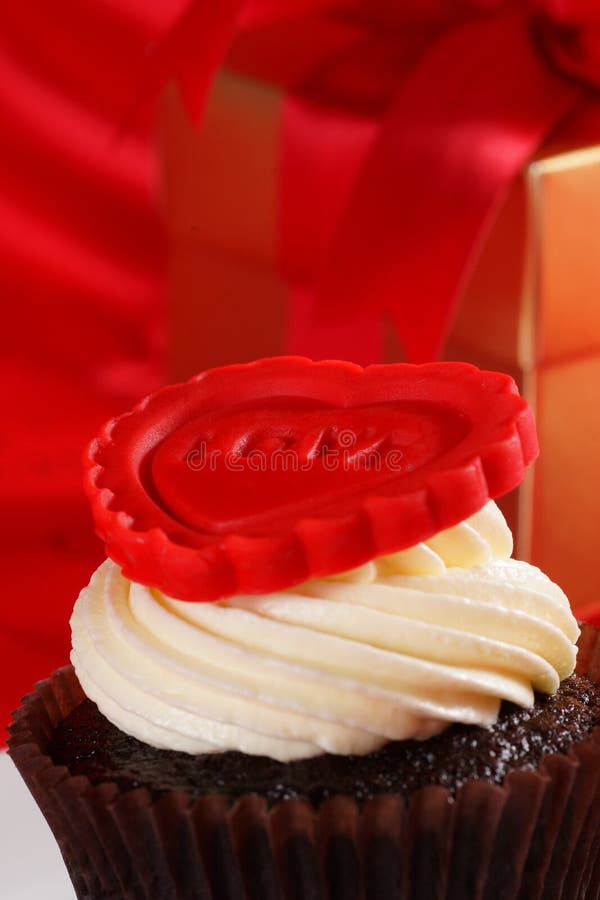 Cupcake with a red heart on top and gifts in boxes on red satin