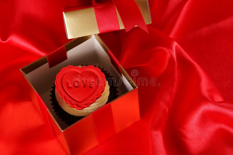 Cupcake with a red heart on top in gifts boxes on red satin back