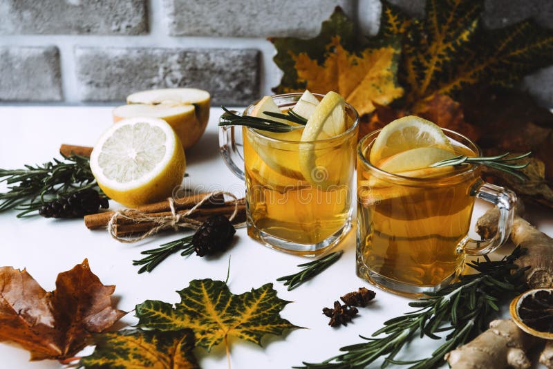 Cups of fruit tea with lemon and orange, rosemary, cinnamon stick, ginger, star anise on a background of maple leaves