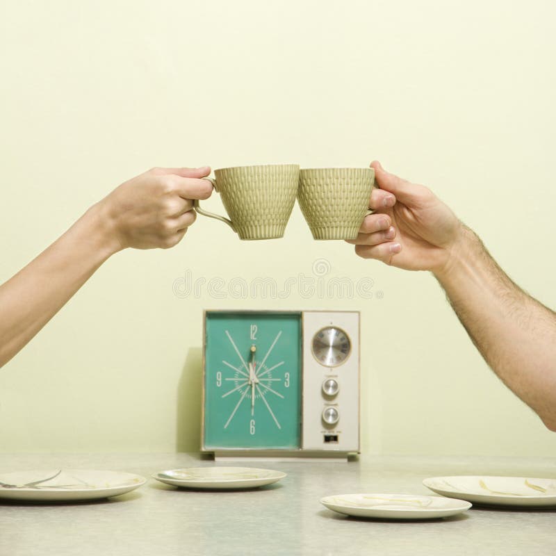 Caucasian male and female hands toasting with coffee cups across retro kitchen table setting. Caucasian male and female hands toasting with coffee cups across retro kitchen table setting.