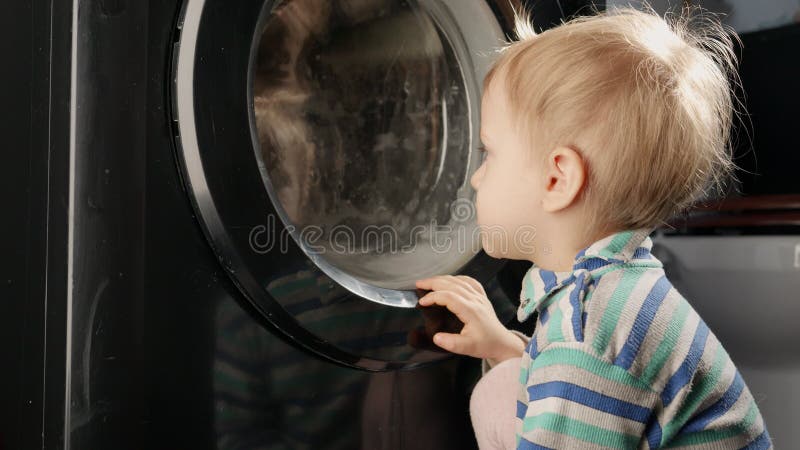 Curioso bebê olhando o tambor rotativo da máquina de lavar em casa. trabalho doméstico e tarefas domésticas